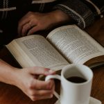 A person sitting on the floor with a book and a cup of coffee