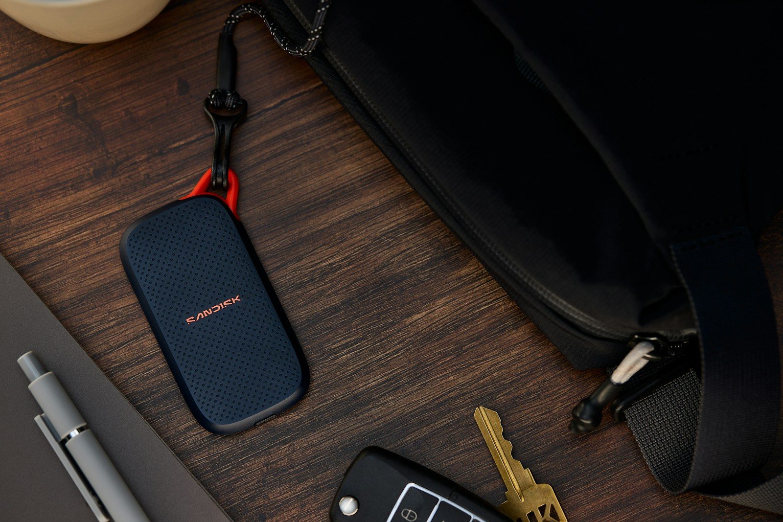 Portable ssd, keys, and pen next to a black bag.